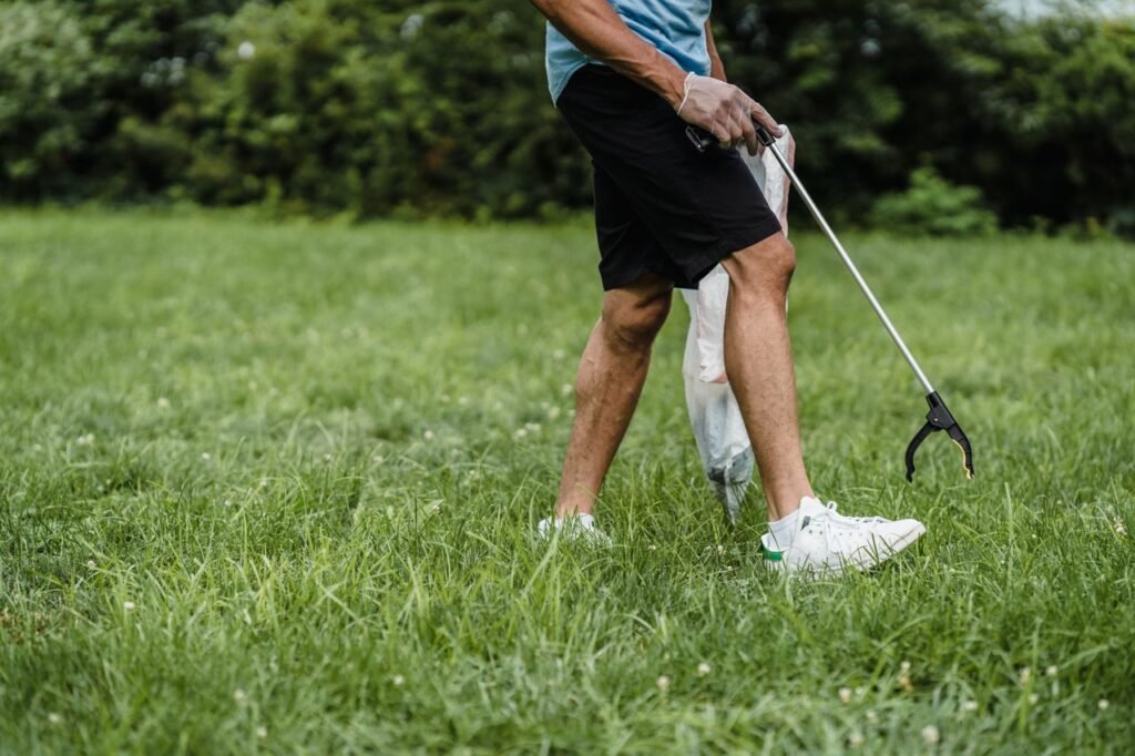 A man picking up plastic waste with gloves in an outdoor park.